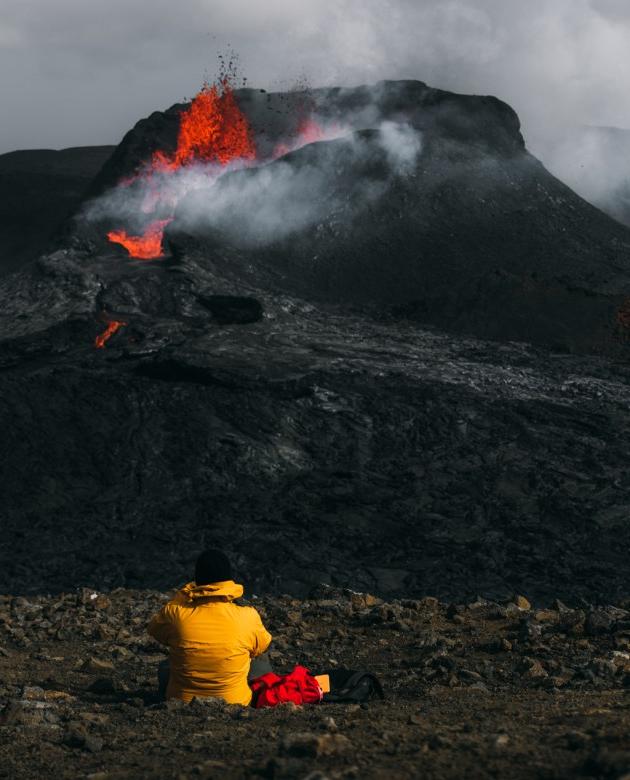 一个穿着黄色冬季夹克的人坐在正在喷发的火山前